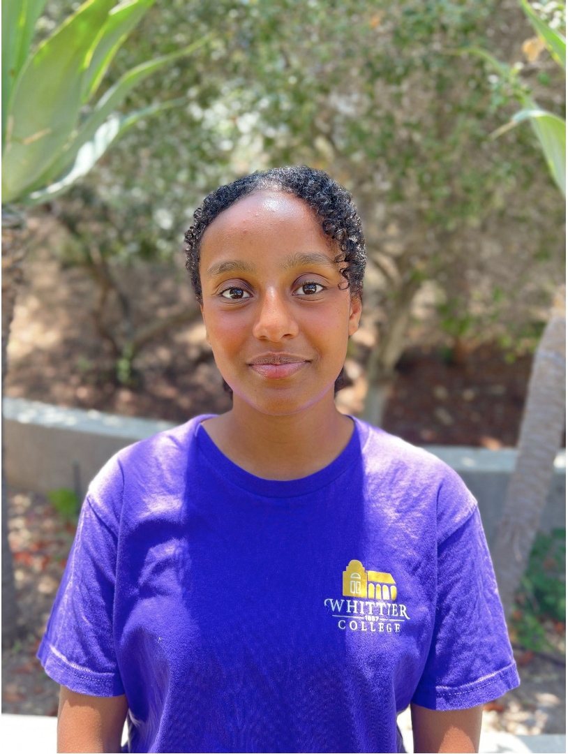 Zion Desta standing in front of plants in Whittier College shirt