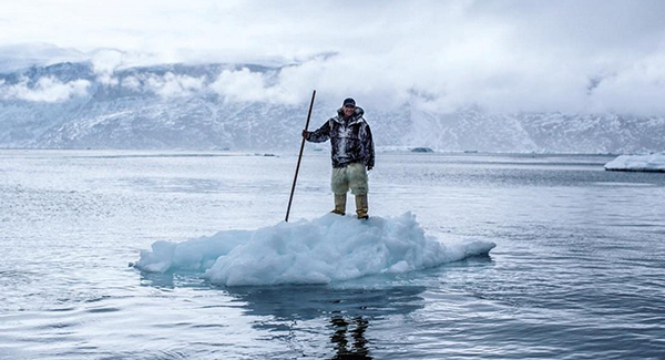 A person stands on top of a floating chunk of ice.
