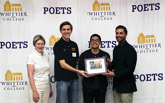 Sharon Herzberger, two male students, and Ian Calderon pose for a photo with a framed group photo.