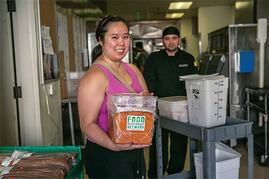 A student holds a tub of food in the back of the cafeteria.