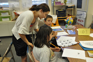 A child development major works with two children at their desks.