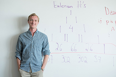 Philip de Castro stands in front of a whiteboard with math equations written on it.