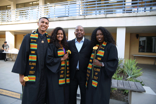 Students in caps and gowns pose with keynote speaker