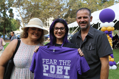 a woman stands to the left of a younger woman holding a purple t-shirt with the words "Fear the Poet." A man stand to the right.