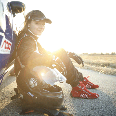 Race Car Driver Natalie Fenaroli sits on the ground with back against her race car