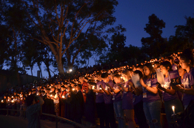 students in the amphitheater holding lit candles