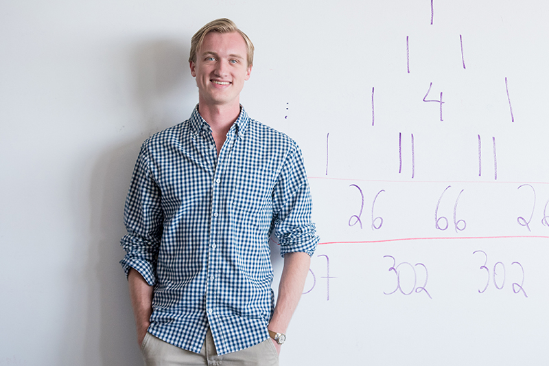 Philip de Castro stands in front of a whiteboard covered in numbers.