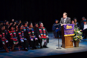 students in caps and gowns listen to keynote speaker at the podium at the Latino commencement