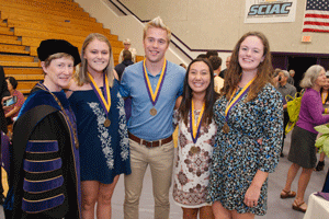 students stand with President Sharon Herzberger inside the Graham Athletic Center
