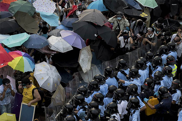 Protestors under umbrellas stand in front of police officers.