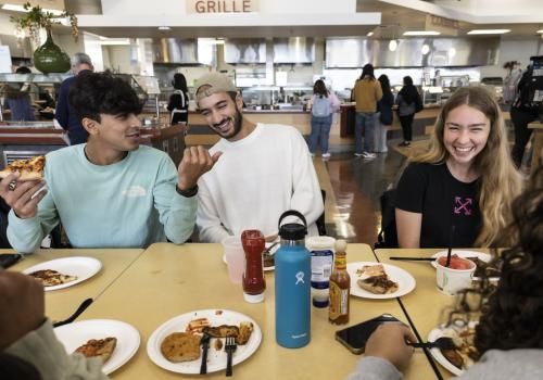 Two male students sitting next to female student laughing in cafeteria