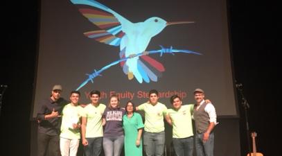 a group of 8 people stand on a stage in front of a screen. on the screen is a projected image of a bird with the words "youth faculty stewardship" underneath