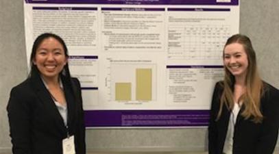 two students stand in front of poster at a conference