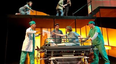 A group of students in medical costumes perform on stage