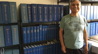 A man stands in front of rows of blue binders stacked on shelves