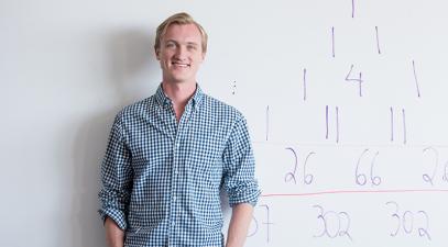 Philip de Castro stands in front of a whiteboard covered in numbers.