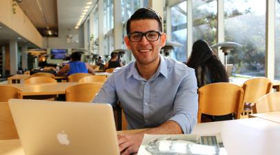 Roberto Bonilla sits on front of his laptop and books in Wardman Library.