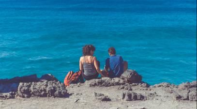 A woman and man sitting in front of the ocean.