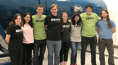 Emi Eastman and seven other people stand in front of a particle accelerator.