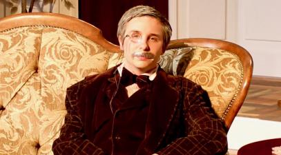 Gunner Joachim sits on a sofa in the costume of his detective character from Gaslight.