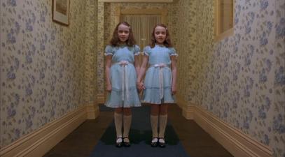 Twin girls in matching dresses stand in hallway in famous scene from the movie, The Shining