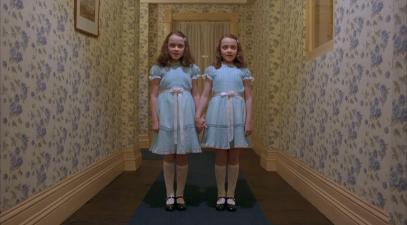 Twin girls in matching dresses stand in hallway in famous scene from the movie, The Shining
